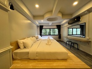 Habitación de hotel con una cama grande, un escritorio con silla y ventana con vista a follaje.