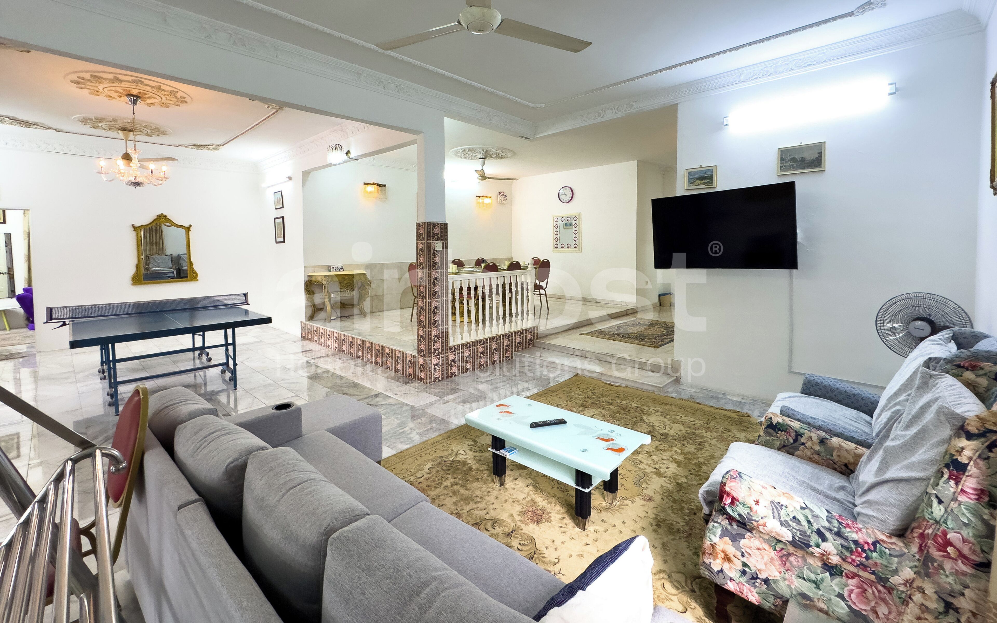 A living room with a sofa, a coffee table, a TV, a ceiling fan, and a dining area with a table and chairs.