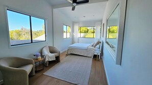 A bedroom with a bed, a chair, a small table, and a large mirror.