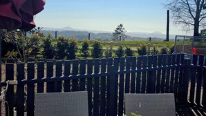 A view from a balcony with a wooden fence, a brick wall, and a distant landscape with mountains.