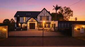 A two-story house with a gated driveway, stone walls, and a well-lit entrance.