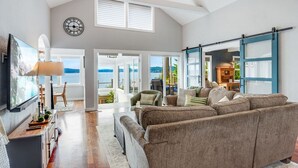 Een ruime woonkamer met een grote bank, een televisie en uitzicht op de omgeving.