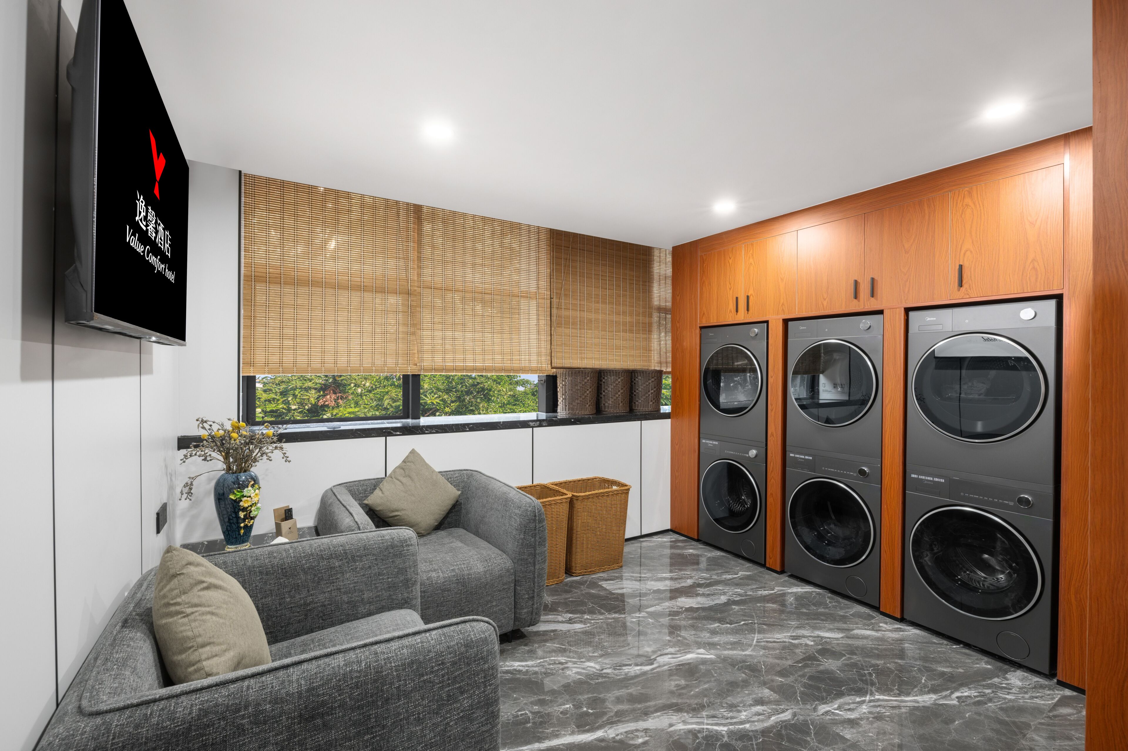 A modern laundry room with four washing machines, a grey sofa, and a television mounted on the wall.