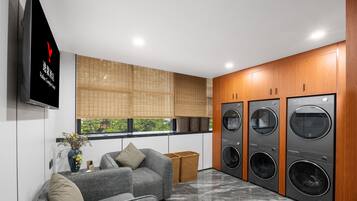 A modern laundry room with four washing machines, a grey sofa, and a television mounted on the wall.