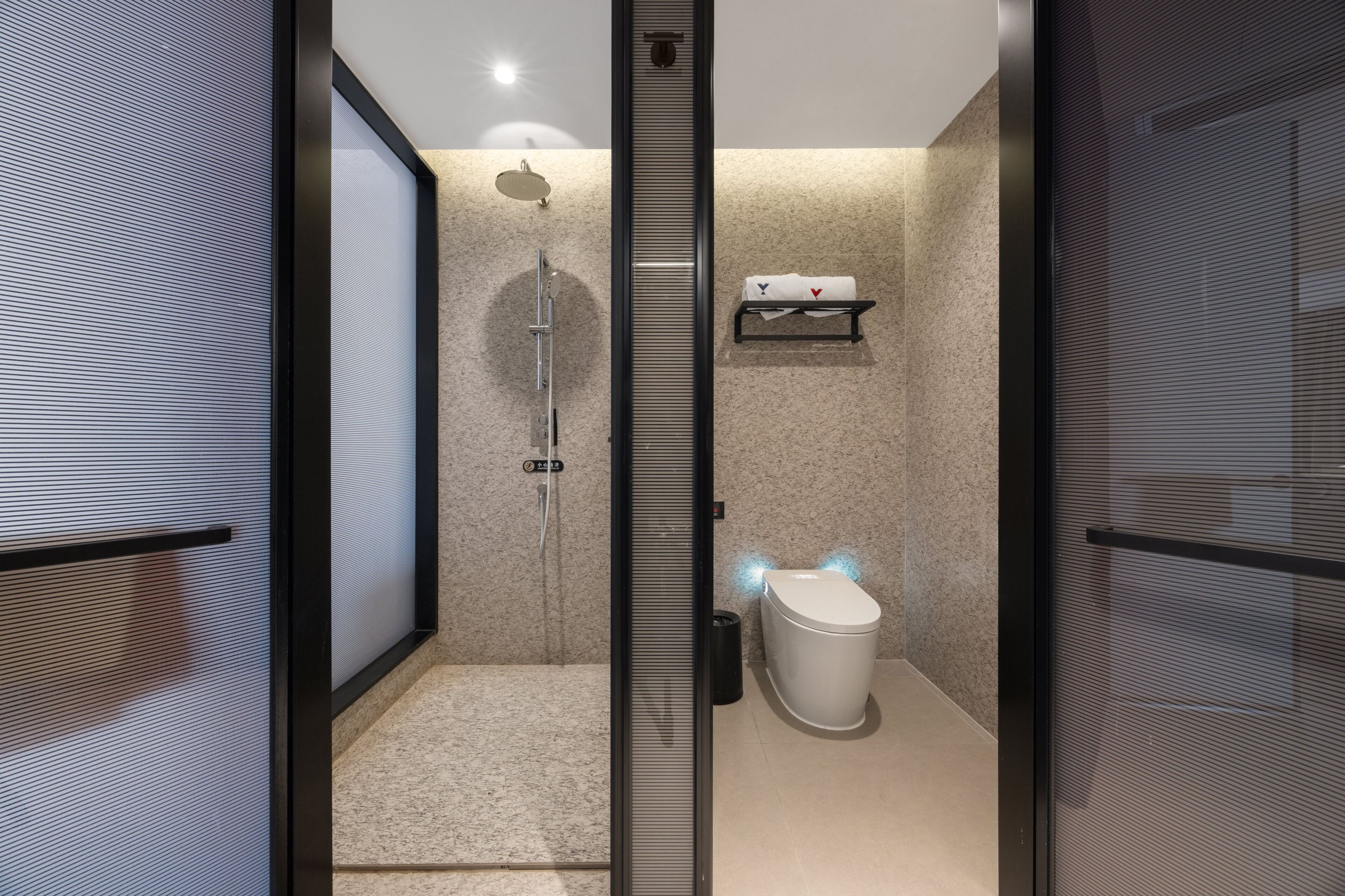 A modern bathroom with a glass partition, a shower, a toilet, and a towel rack.