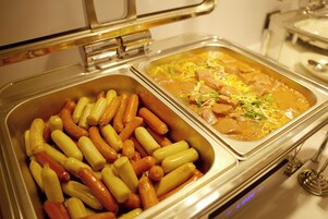 Ein Buffet mit verschiedenen Speisen, darunter Hot Dogs und ein Eintopf mit Fleisch und Gemüse.