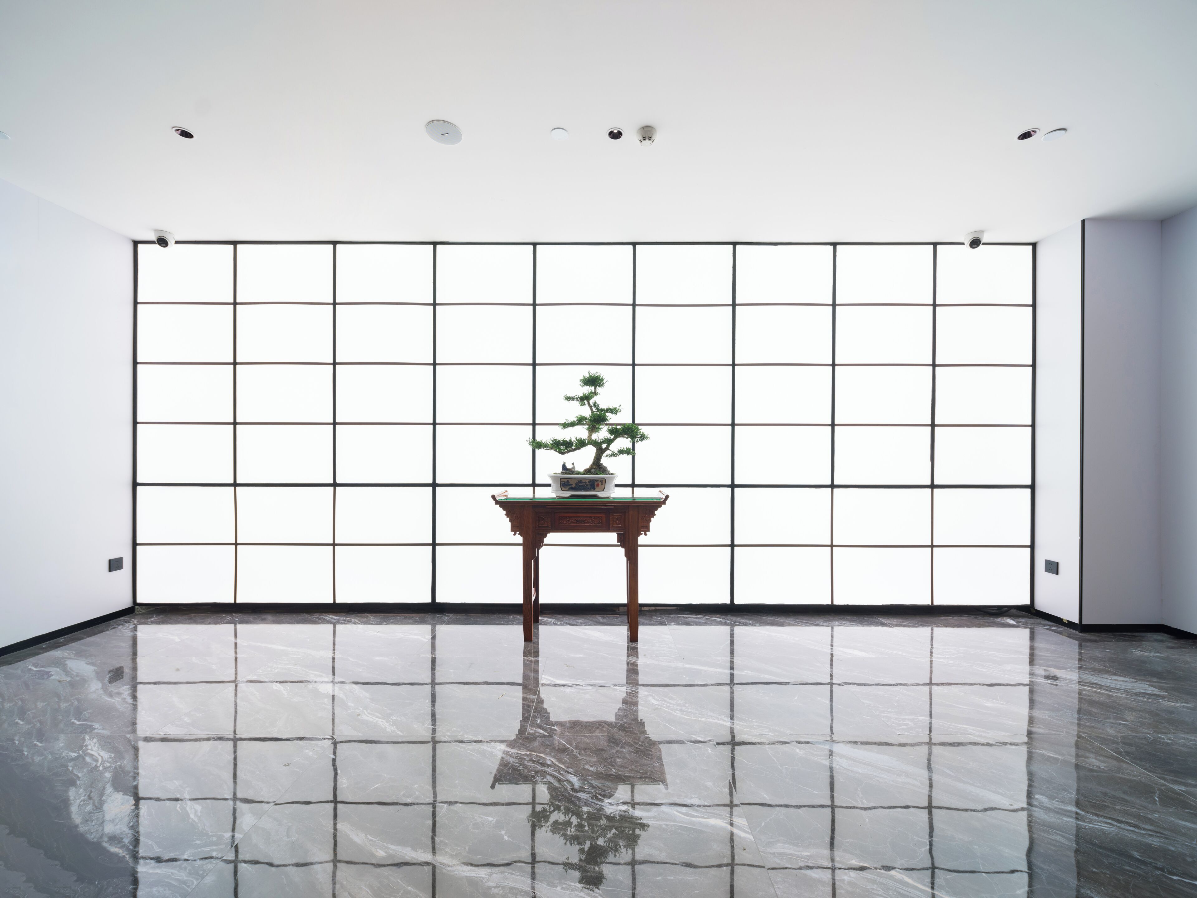 Ein geräumiger Raum mit poliertem Boden, einem traditionellen japanischen Tisch mit einer Bonsai-Pflanze und einer großen Wand mit Gittermuster.