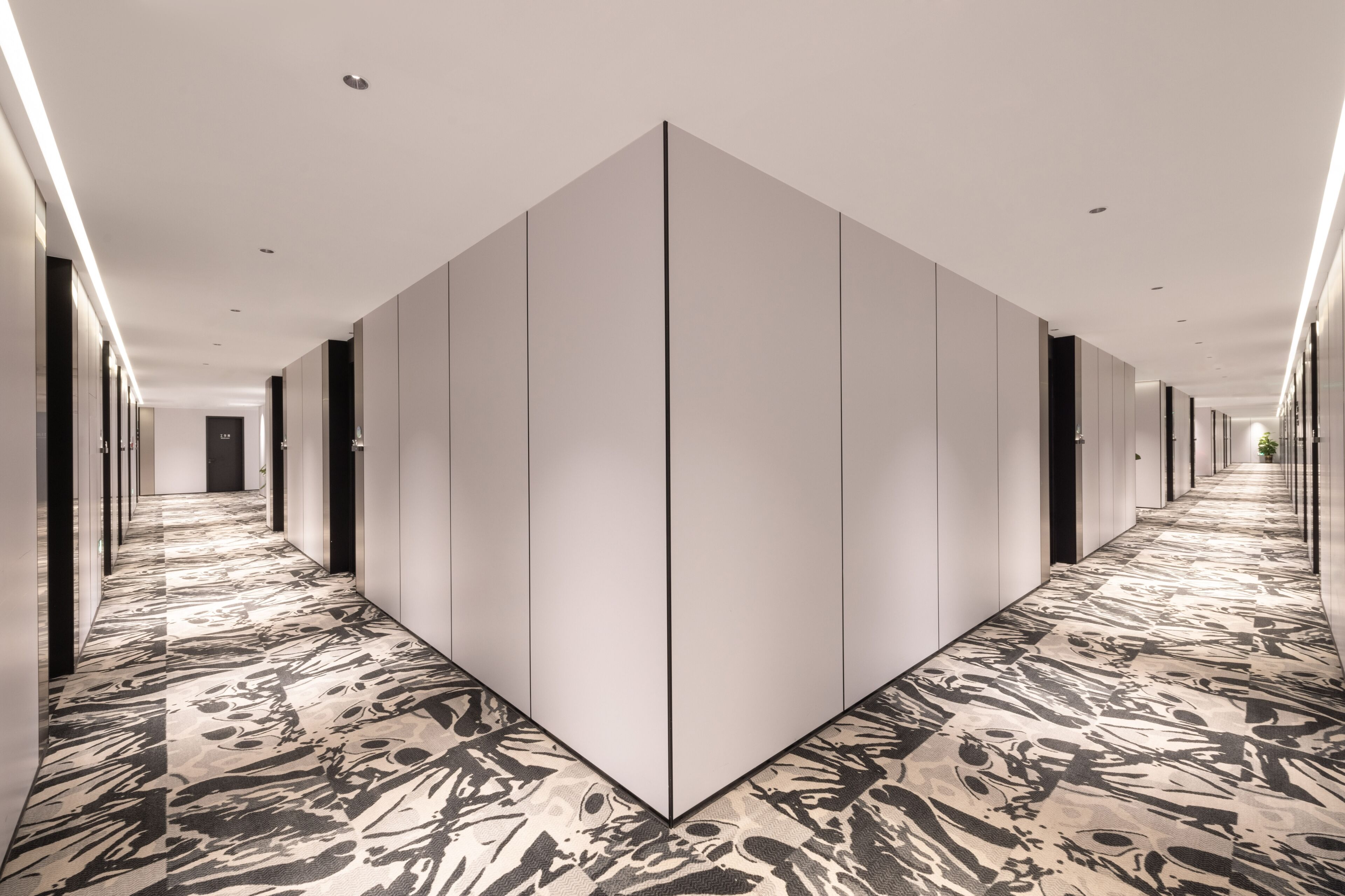 Un long couloir étroit, doté d’un sol à motifs, de murs blancs et d’une cloison centrale.