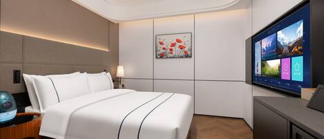 A modern hotel room with a bed, bedside table, lamp, artwork, and a large screen displaying room options.