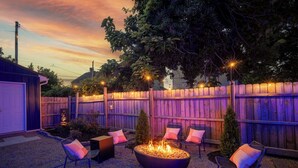 An outdoor patio area with a fire pit, seating, and a wooden fence. - Backyard Escape: Outdoor Movie, Dome, Mini Golf, hot tub, fire pit, grill, mural (Columbus)
