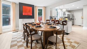 A modern kitchen with white cabinets, a central island, and a dining area with a wooden table and chairs. - Backyard Escape: Outdoor Movie, Dome, Mini Golf, hot tub, fire pit, grill, mural (Columbus)
