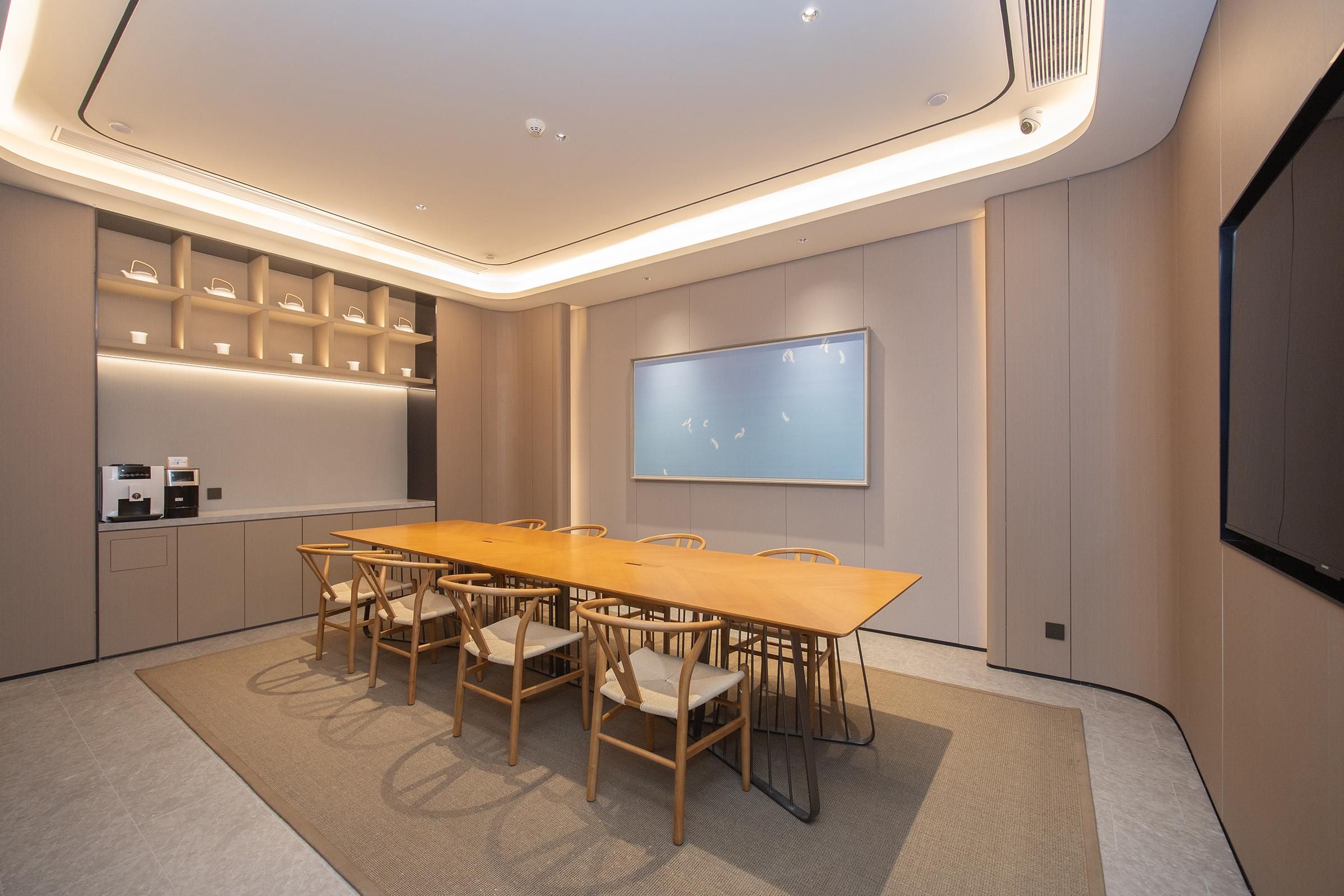 A conference room with a long wooden table, six chairs, a projector screen, and built-in shelves with lighting.