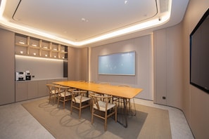 A conference room with a long wooden table, six chairs, a projector screen, and built-in shelves with lighting.