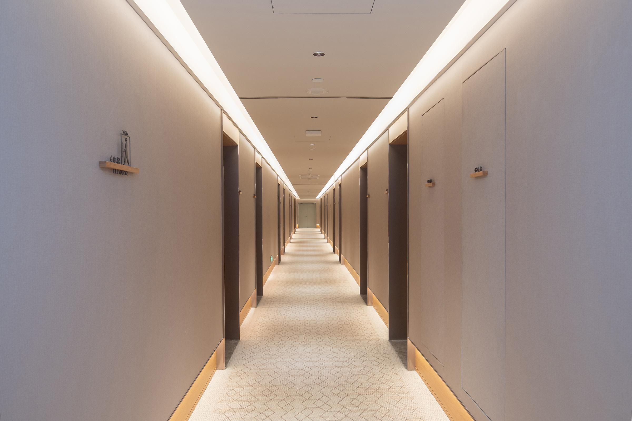 A long, narrow hallway with a patterned carpet and recessed lighting.