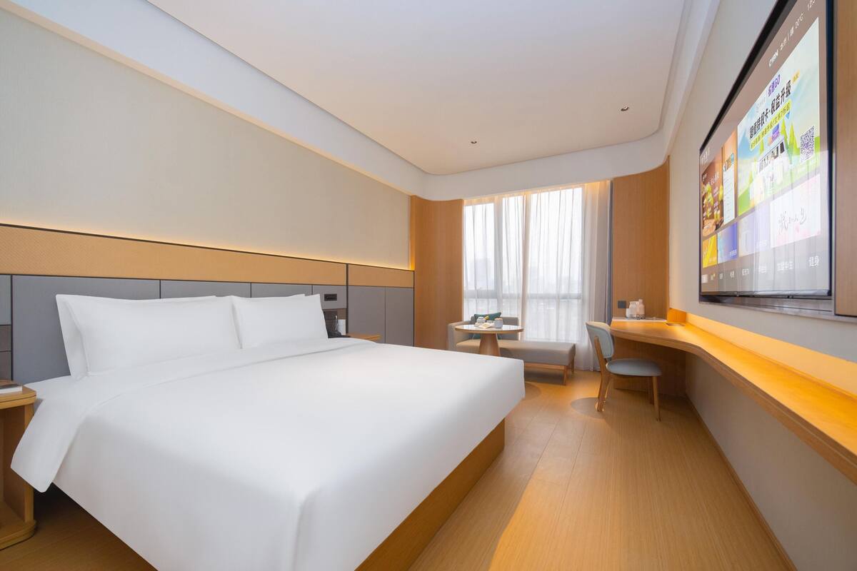 A hotel room with a large bed, a desk, and a TV mounted on the wall.