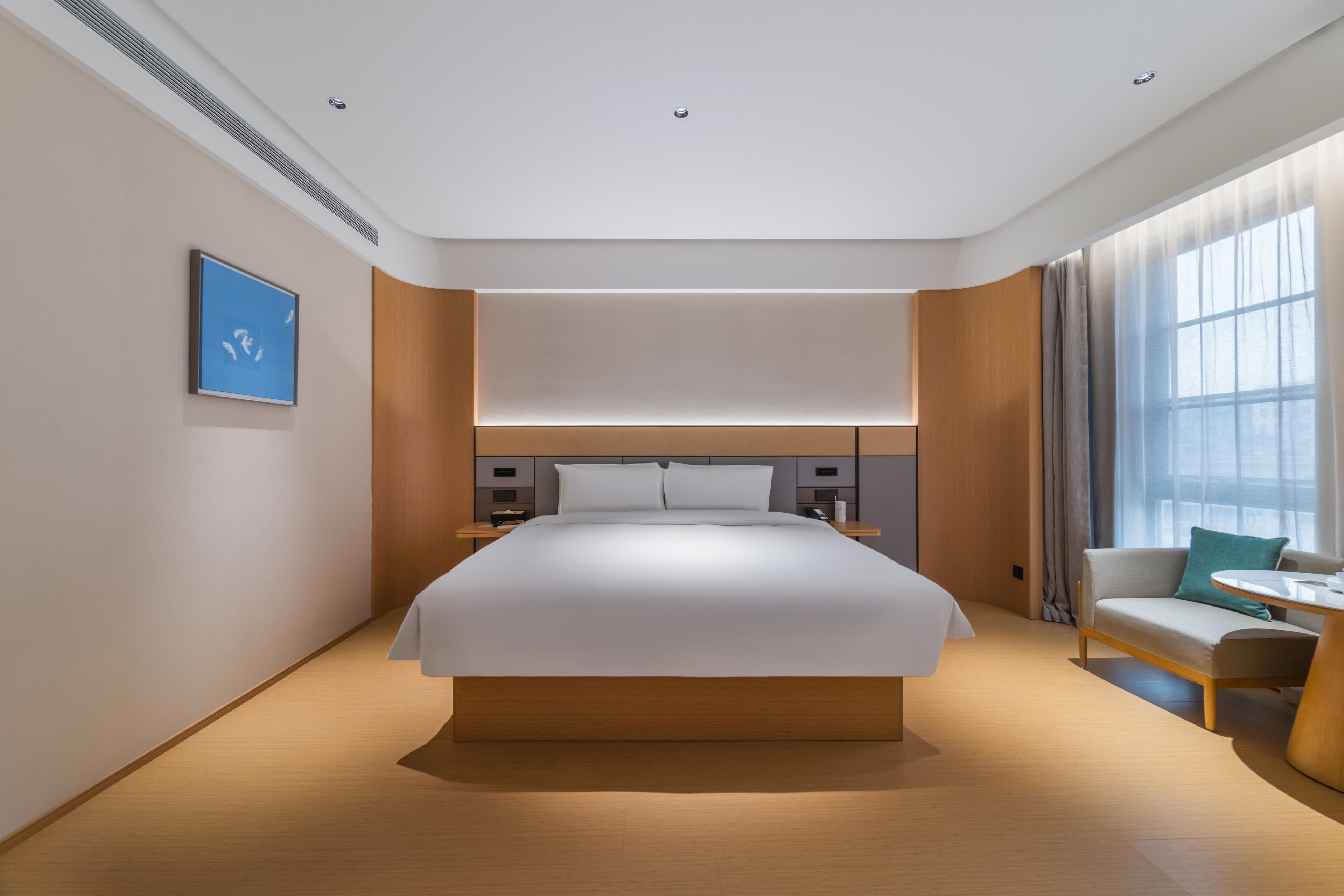 A modern hotel room with a large bed, bedside tables, a sofa, and a window with curtains.