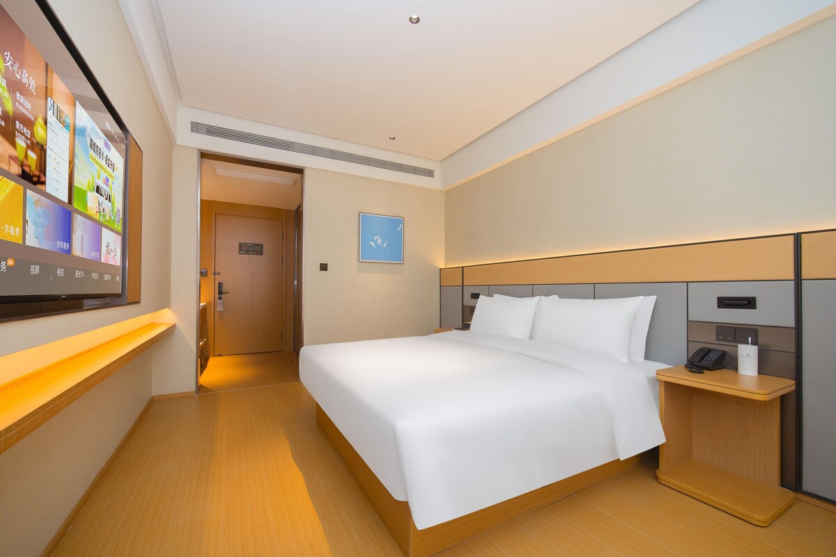 Une chambre d’hôtel avec un grand lit, une table de chevet avec un téléphone, un téléviseur fixé au mur et une porte donnant sur une autre pièce.