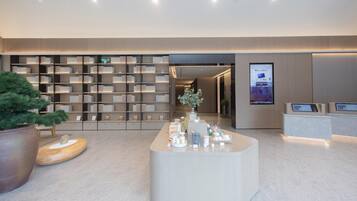 A modern interior with a reception desk, a large bookshelf, and a potted plant.
