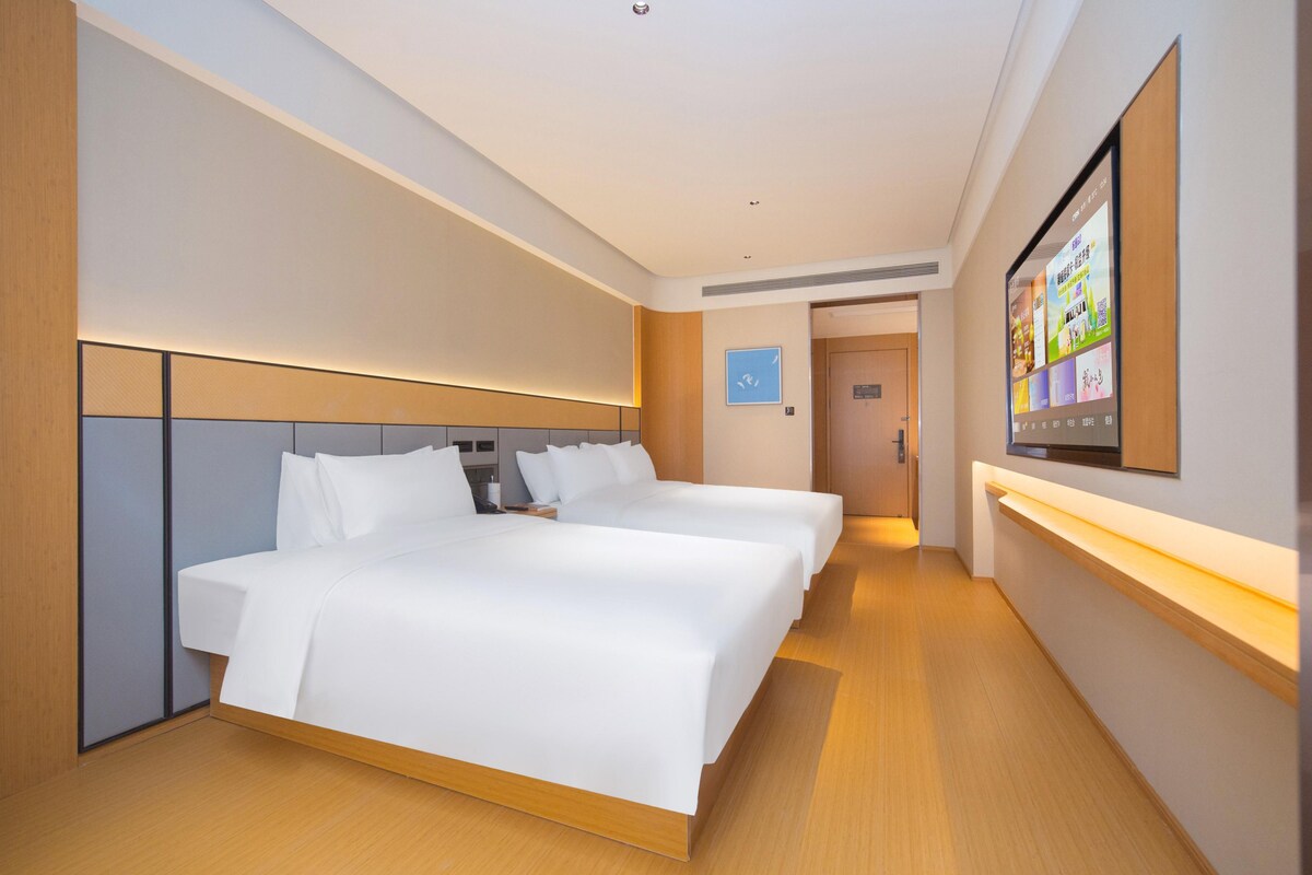 A modern hotel room with a large bed, a TV mounted on the wall, and a wooden floor.
