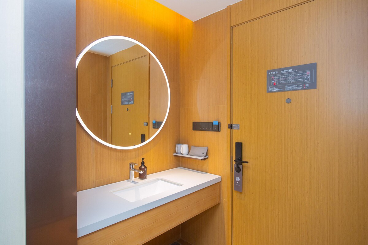 A modern bathroom with a wooden vanity, a round mirror, a sink, and a toilet.