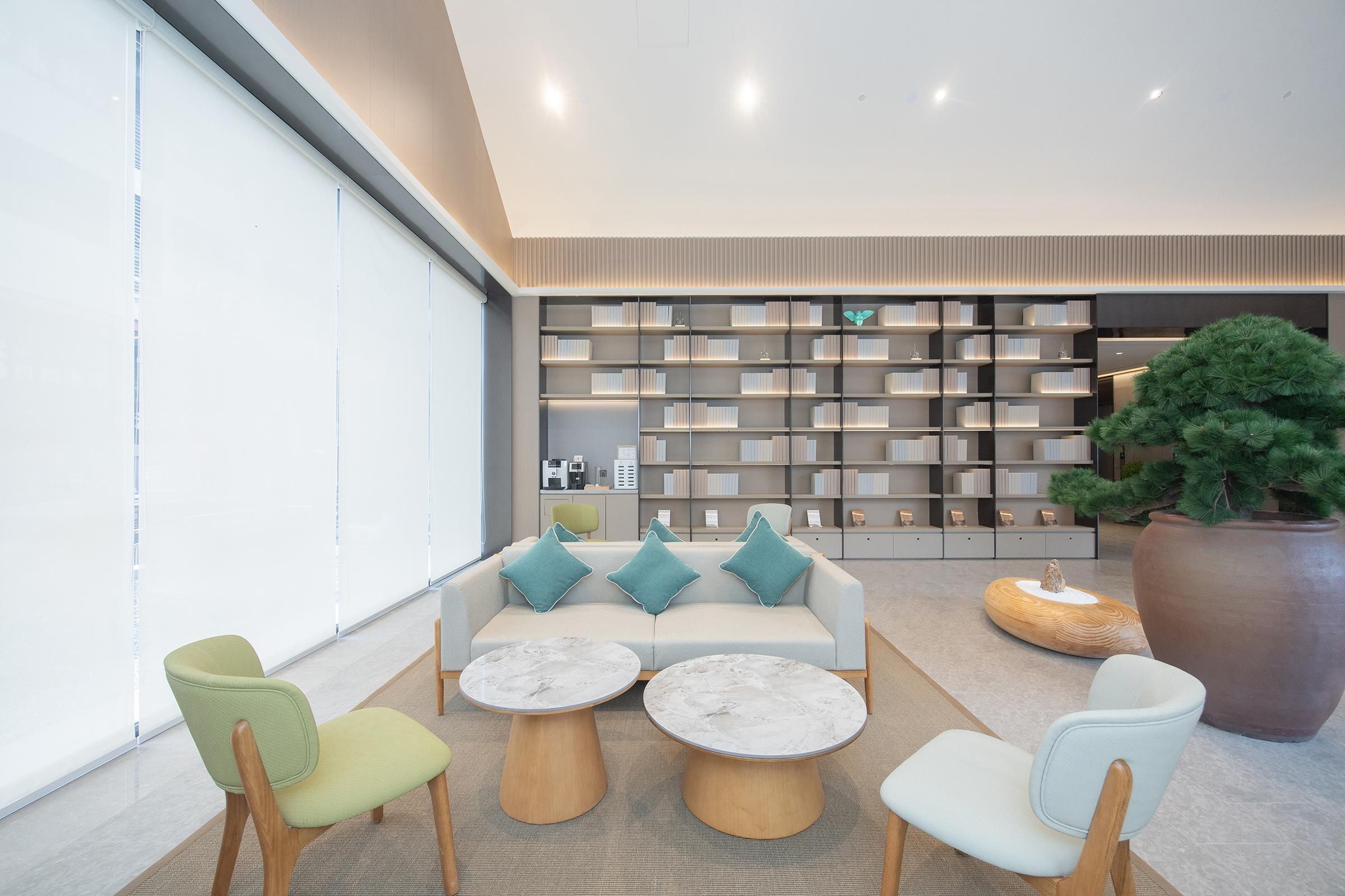 A modern lounge area with a sofa, two round tables, and a large bookshelf in the background.