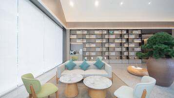 A modern lounge area with a sofa, two round tables, and a large bookshelf in the background.