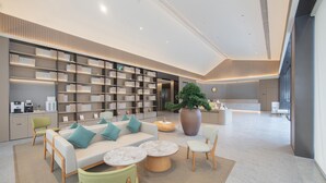A modern, well-lit lounge area with a sofa set, coffee table, and seating, surrounded by bookshelves and a large potted plant. - Ji Hotel Guangzhou Baiyun Station Sanyuanli Avenue (Guangzhou)