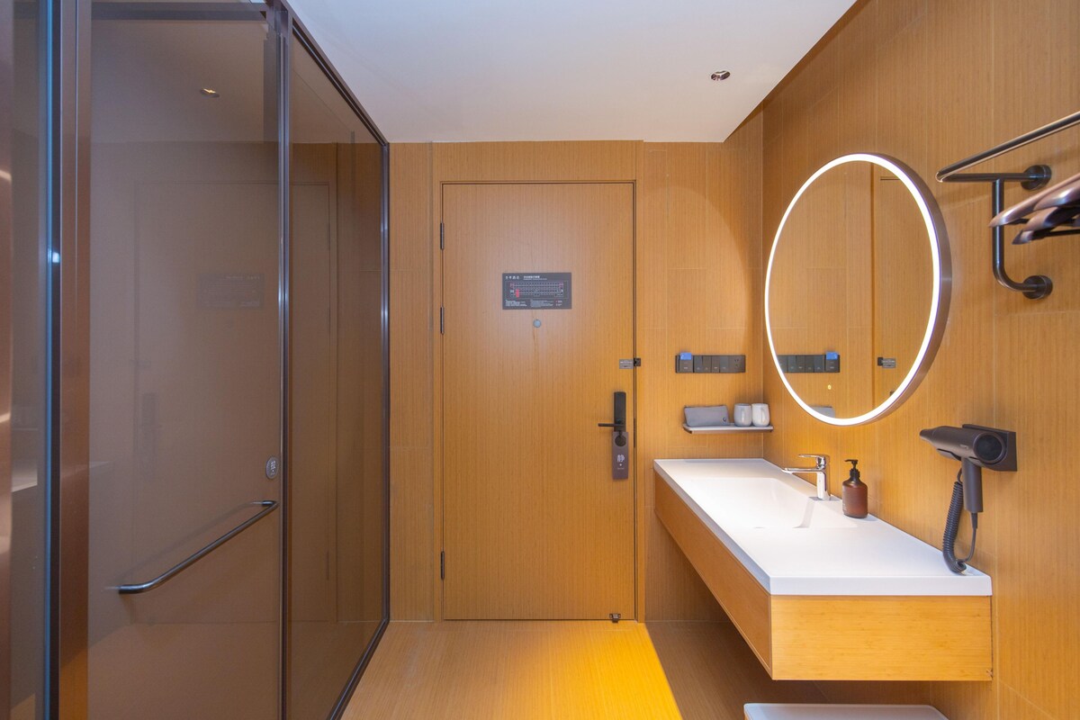 Une salle de bain moderne avec une porte en bois, un lavabo blanc, un miroir avec un éclairage intégré et un porte-serviettes.
