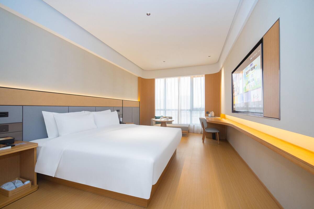 A hotel room with a large bed, a desk, a chair, and a window with curtains.