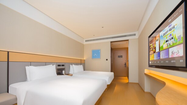 Une chambre d’hôtel avec deux lits, un téléviseur fixé au mur et un banc en bois.
