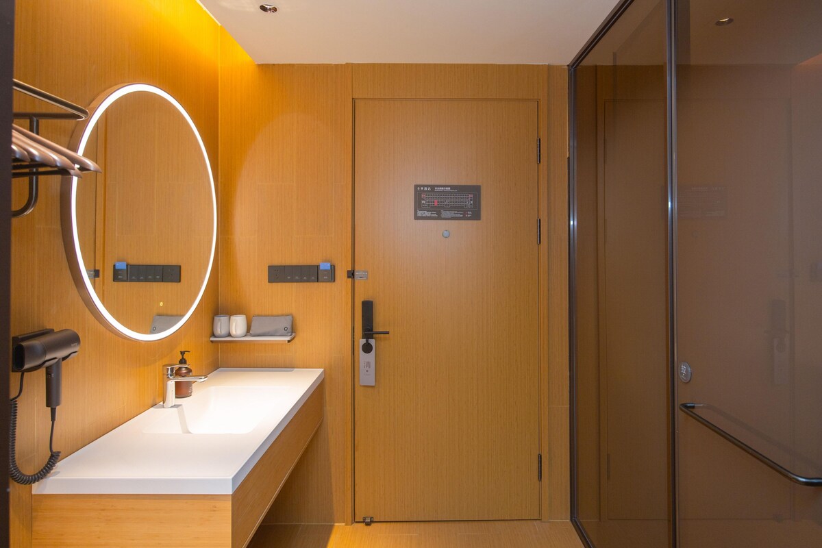 A modern bathroom with a wooden vanity, a mirror with a light, a hairdryer, and a shower area.