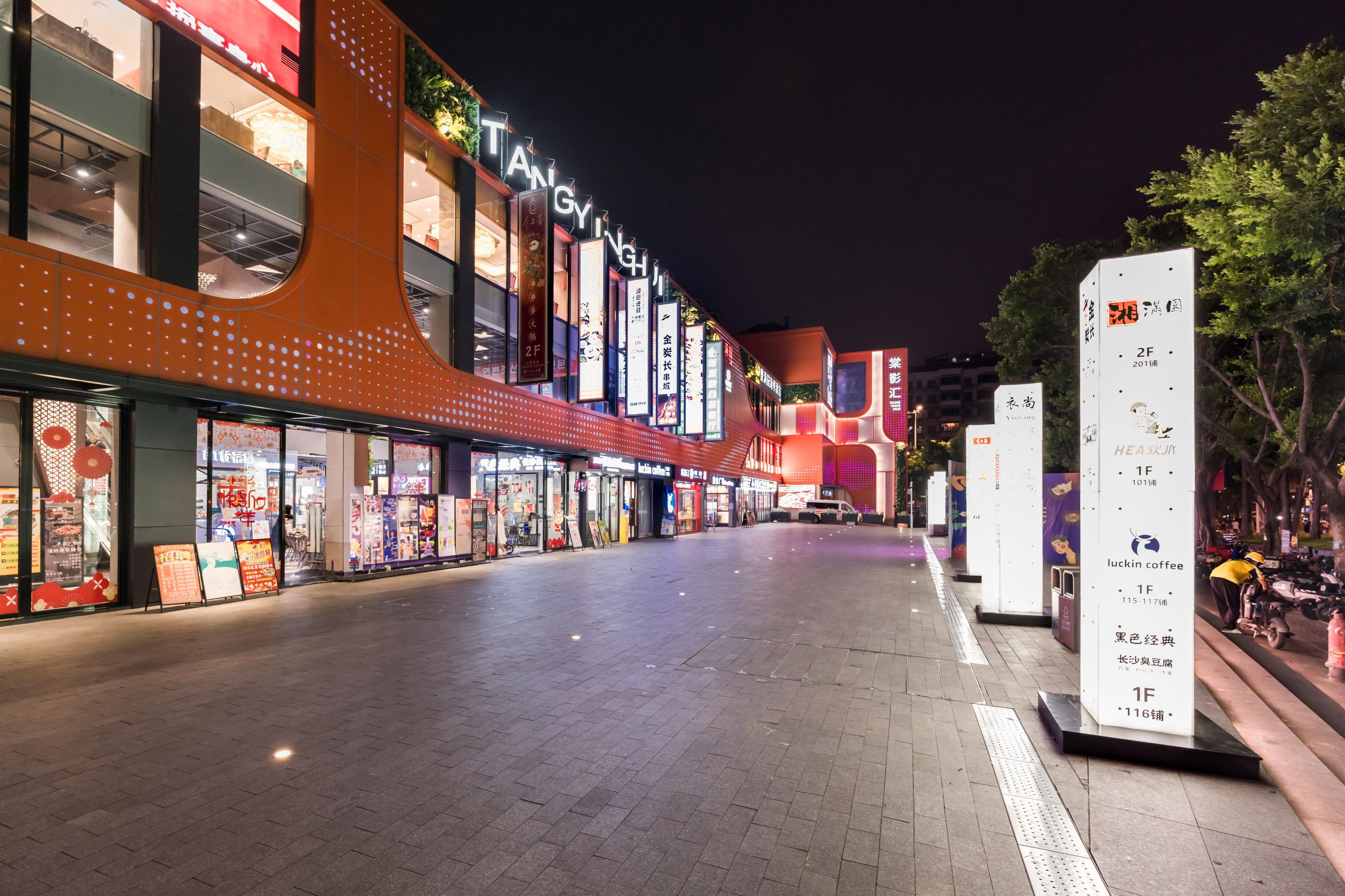 A brightly lit commercial street with illuminated storefronts and signage.