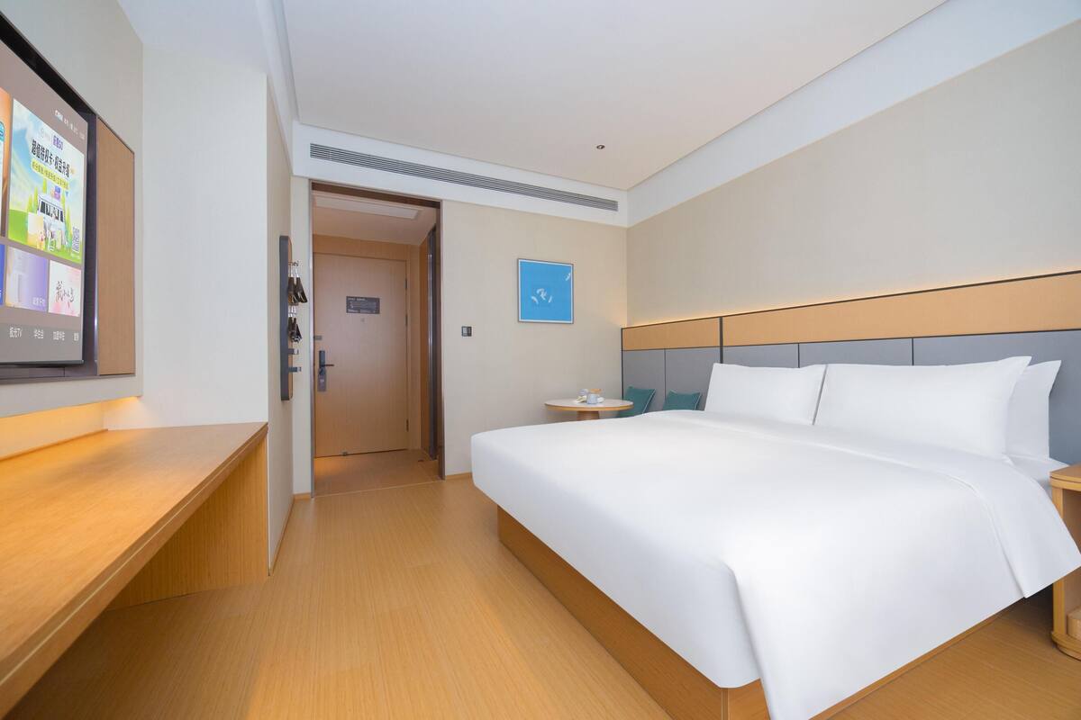 A hotel room with a large bed, bedside tables, a TV mounted on the wall, and a door leading to another room.