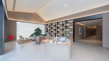 A modern hotel lobby with a reception desk, seating area, and a large potted plant.