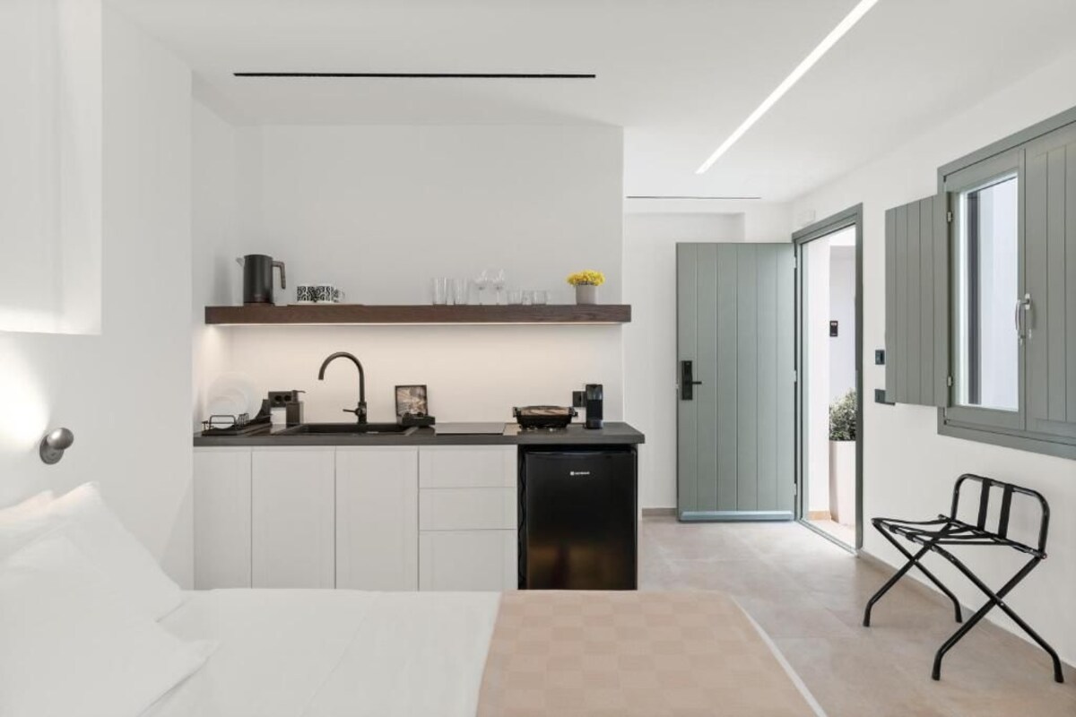 Una habitación de hotel moderna con kitchenette, una cama, una pequeña zona de estar y vistas a través de una puerta abierta.
