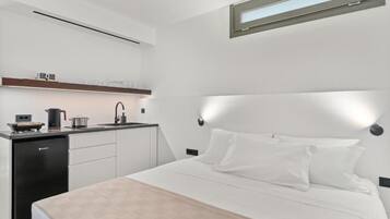 Een moderne hotelkamer met een bed, nachtkastje en een klein kitchenette.