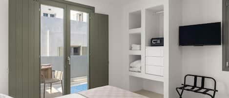 Ein Hotelzimmer mit Bett, einem an der Wand montierten Fernseher, einem Sessel und einem Balkon mit Stadtblick.