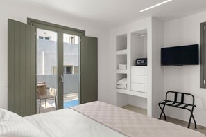 Ein Hotelzimmer mit Bett, einem an der Wand montierten Fernseher, einem Sessel und einem Balkon mit Stadtblick.
