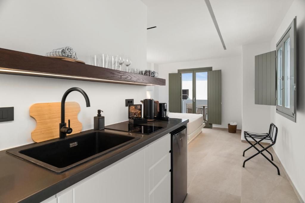 Una cocina moderna con un lavamanos negro, armarios blancos y una tabla de cortar de madera. Hay una cafetera y un refrigerador pequeño sobre la encimera.