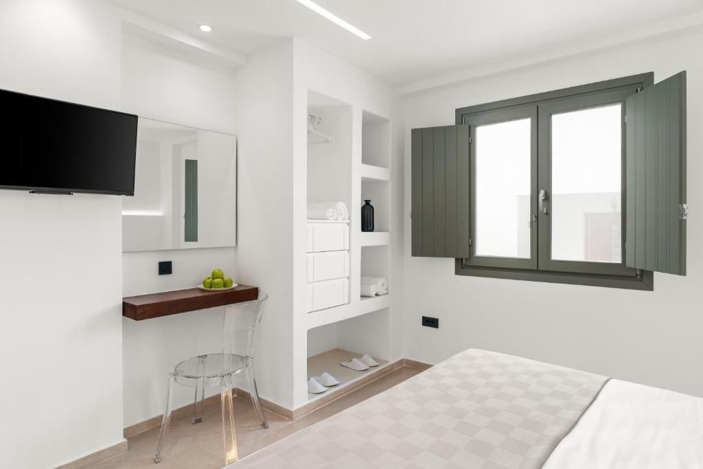Quarto moderno com cama, televisão fixada na parede, mesa pequena com cadeira e janela com persianas.