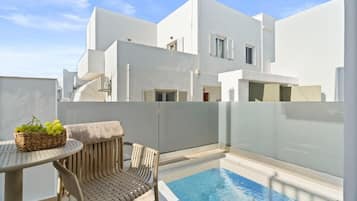 Um edifício moderno branco com piscina, uma mesa de vime com uma cesta de uvas e uma cadeira de vime.