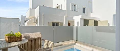 Un edificio moderno blanco con piscina, una mesa de mimbre con una cesta de uvas y una silla de mimbre.