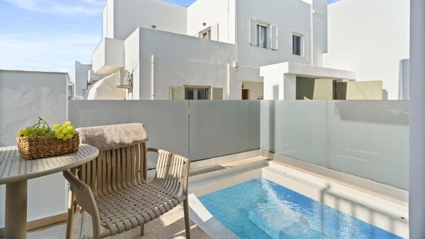 Um edifício moderno branco com piscina, uma mesa de vime com uma cesta de uvas e uma cadeira de vime.