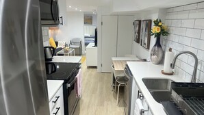 Eine moderne Küche mit einem Edelstahlkühlschrank, einem Einbauofen und einer Spüle mit Armatur. Es gibt einen Essbereich mit Tisch und Stühlen sowie eine kleine Kücheninsel mit einer Blumenvase.