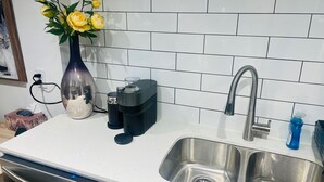 Eine Küche mit Spüle aus Edelstahl, einer Kaffeemaschine und einem Blumenstrauß mit gelben Blumen auf der Arbeitsfläche.