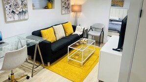 Ein modernes Wohnzimmer mit einer schwarzen Couch, gelben Kissen, einem Glastisch und einem weißen Sessel.
