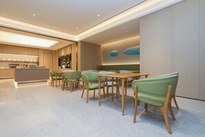 Un comedor moderno con una mesa central y sillas, una cocina al fondo y un suelo de tonos claros.