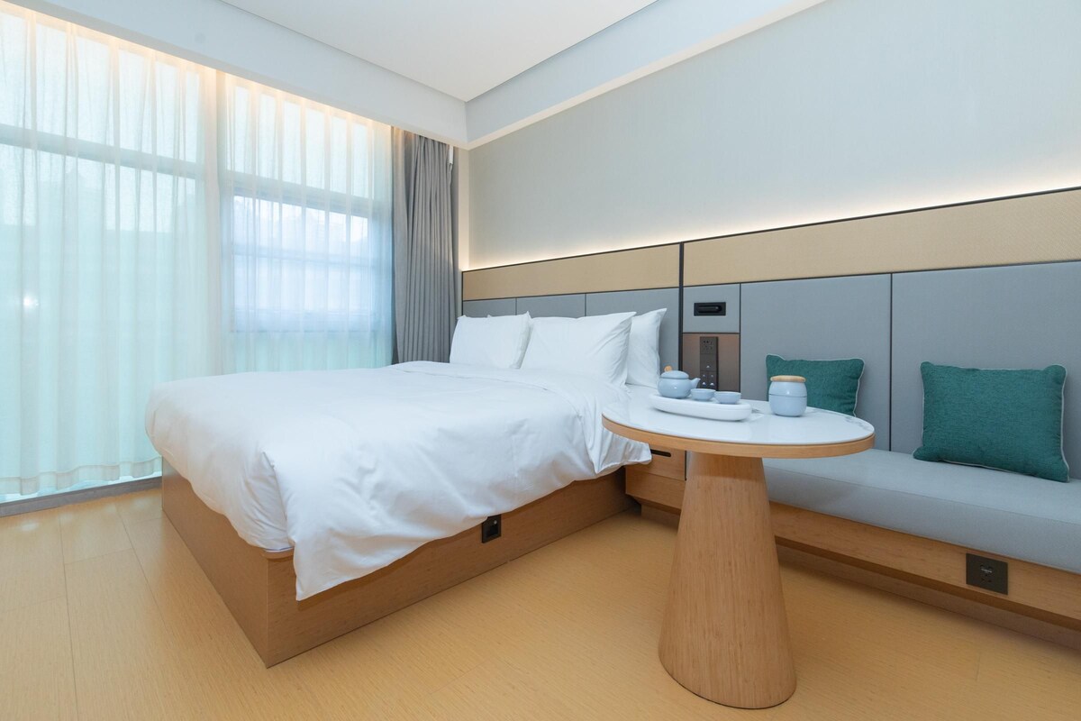 Una camera d'albergo moderna con un letto, un tavolino rotondo in legno e un angolo relax con cuscini.
