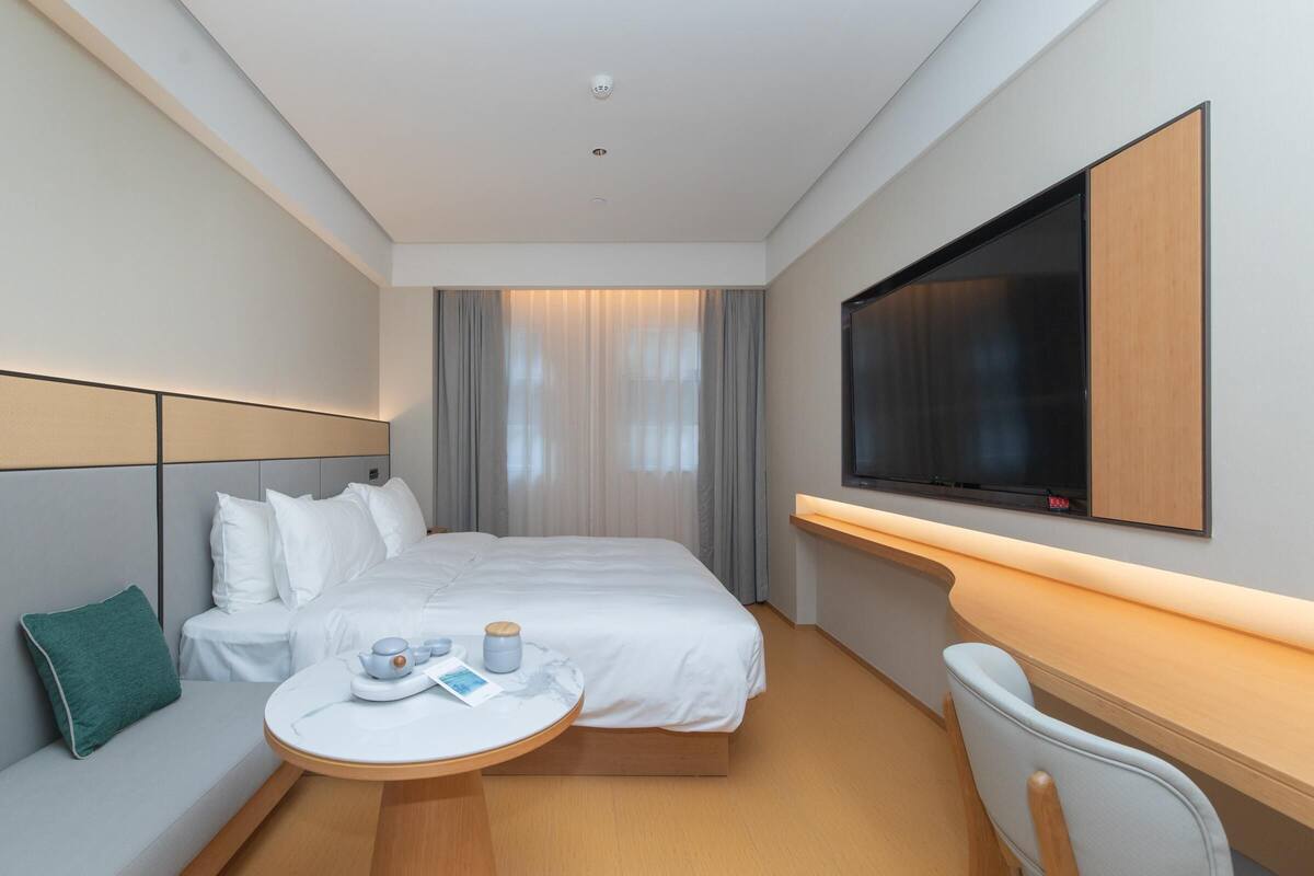 A hotel room with a bed, bedside table, TV, and a seating area with a chair and table.