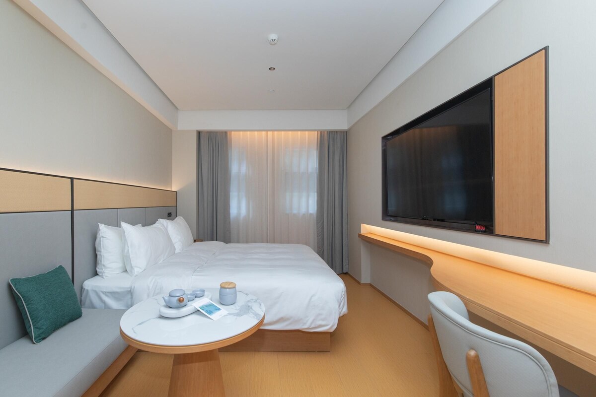 A hotel room with a bed, bedside table, TV, and a seating area with a chair and table.